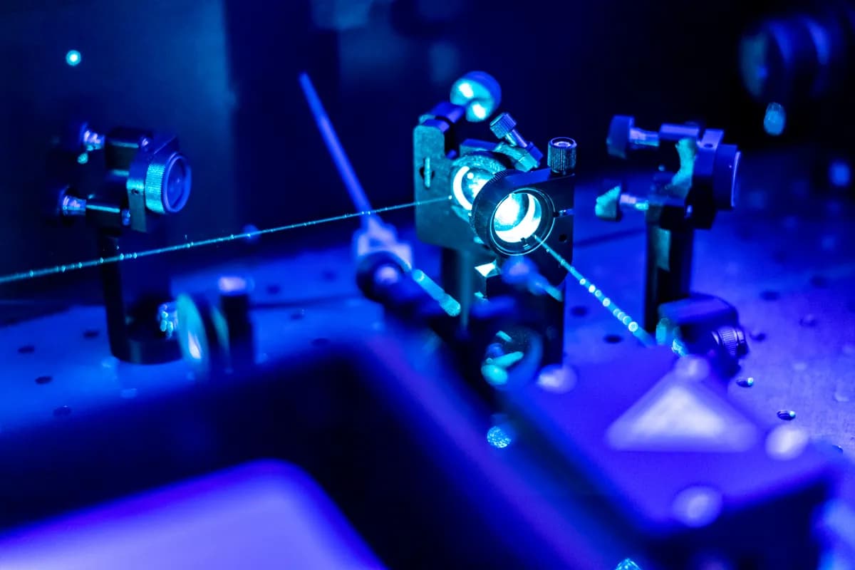 A blue laser beam crossing an optical bench through mounted lenses and mirror mounts